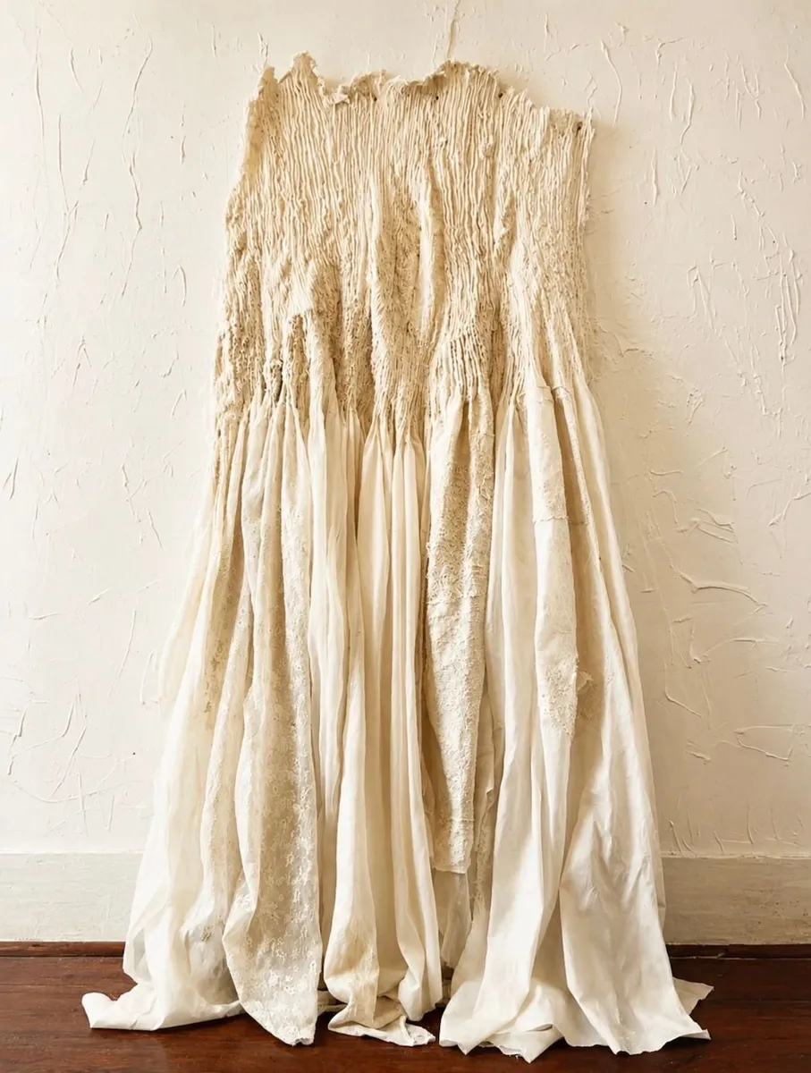 ELIANE DUARTE — VESTIDO DE NOIVA, 1994

Tecido e bordados costurados
262 × 100 × 60 cm
Coleção João Sattamini / comodato MAC Niterói

Vestido de Noiva concentra uma tensão central na obra de Eliane Duarte: aquilo que remete à intimidade, ao feminino e à tradição doméstica é submetido a um processo de transformação material. O vestido deixa de ser vestimenta para tornar-se corpo — simultaneamente abrigo, pele, memória e estranhamento.

Em texto dedicado à artista no contexto da Coleção Sattamini, a crítica identifica em sua produção uma combinação de artesania e visceralidade: é no confronto direto com os materiais que emerge sua carga simbólica. A costura parece fazer nascer organismos em gestação e formas em metamorfose, como se algo estivesse permanentemente tentando adquirir outro corpo.

A própria inserção de Vestido de Noiva no acervo Sattamini/MAC permite outra leitura curatorial: em uma reflexão museológica sobre a coleção, a obra aparece no núcleo dedicado ao tecido, explorando a relação entre tecer e texto, processo e matéria, ao lado de trabalhos de Katie van Scherpenberg, Artur Barrio e Cildo Meireles.